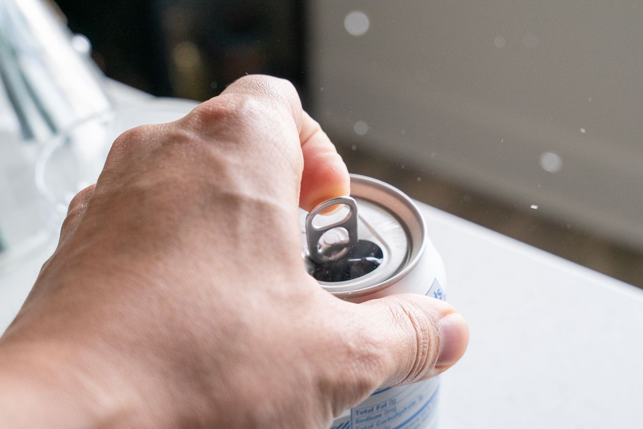 hand opening a plain soda can
